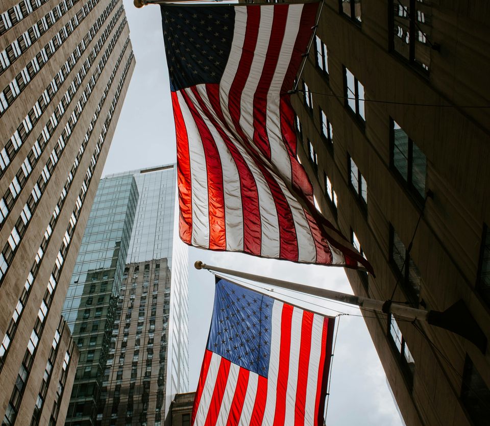 Dos banderas de Estados Unidos colgadas entre los edificios de Rockefeller Center, vistas desde abajo.